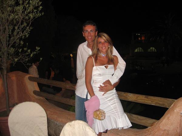 Couple dressed in white embracing at night beside a wooden railing
