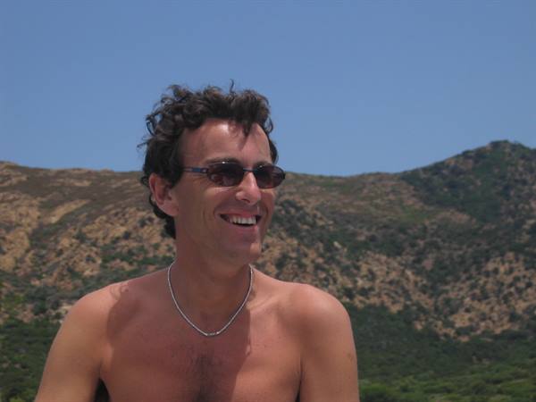 Shirtless man in sunglasses smiling in front of arid hills