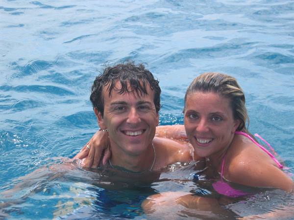 Smiling couple in blue water, she hugs him wearing pink bikini