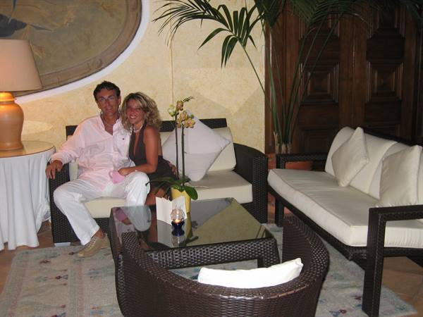 Man and woman sit on rattan sofas with white cushions in a lounge with orchid