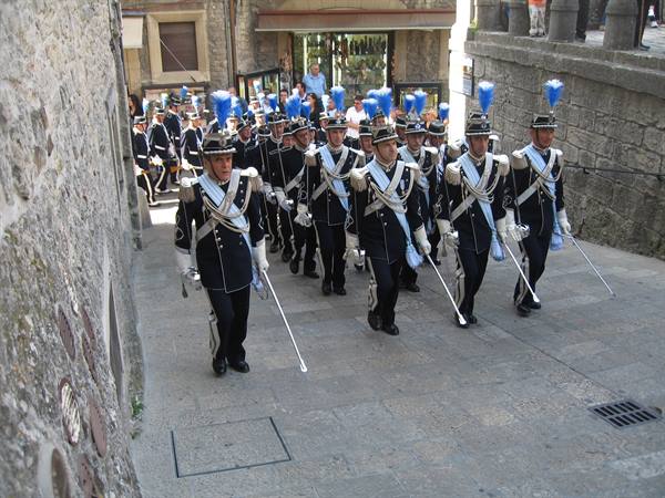 San Marino guard in dark uniforms with blue plumes marches down the stone steps