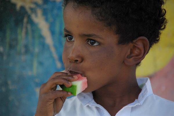 Child biting a watermelon slice in front of a painted wall