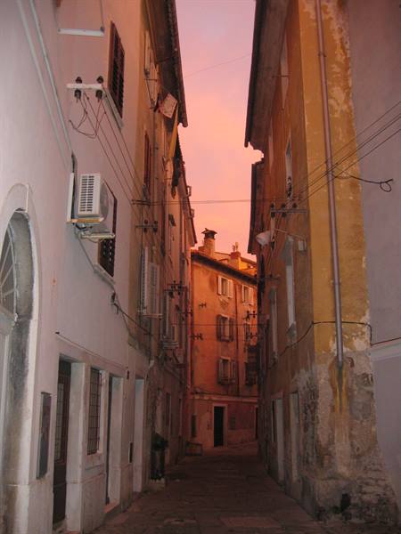 Narrow alley between old buildings with wires and air conditioners, pink sky
