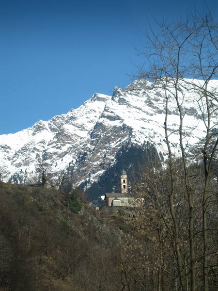 Church with bell tower framed by bare branches, snowy mountain and blue sky behind