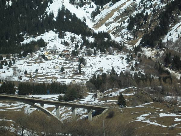 Concrete bridge over snowy slope, village houses scattered among firs