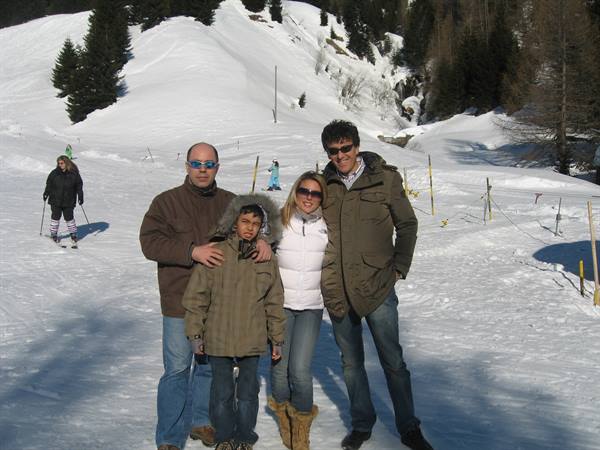 Family with child posing on snow, snowy ski slopes and skiers behind