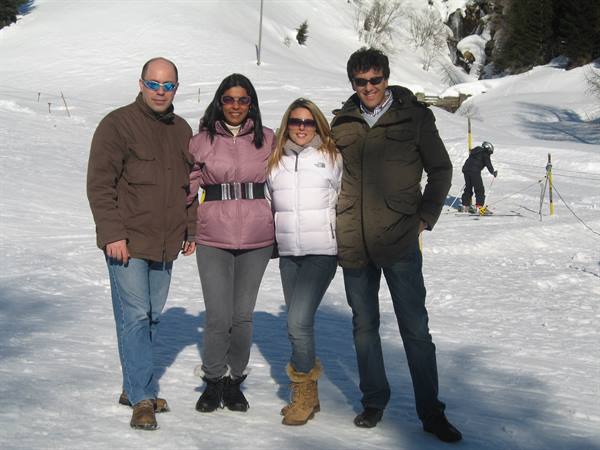 Four friends wearing sunglasses pose on the snow of a ski slope
