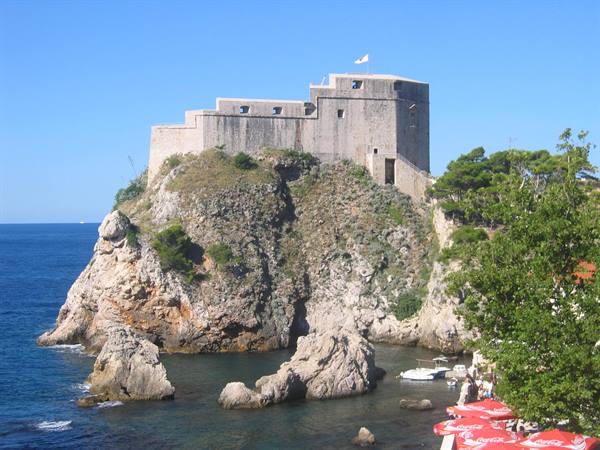 Lovrijenac Fortress on rocky cliff, red umbrellas below, Dubrovnik