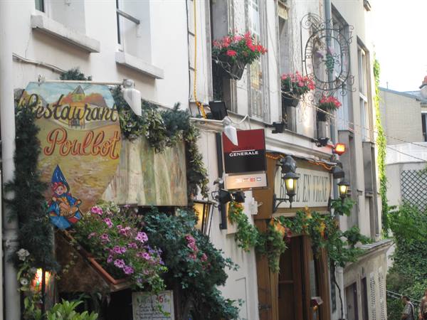 Poulbot restaurant sign in Montmartre, flowers hanging over narrow lane
