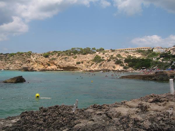 Turquoise cove with swimmers among rocks and pines, hotel on the cliff