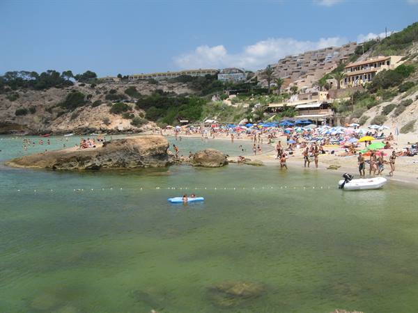 Crowded beach with colorful umbrellas, rocks, inflatable boats and swimmers in green water