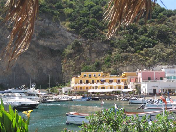 Boats in Sant'Angelo harbor, colorful houses beneath the green cliff
