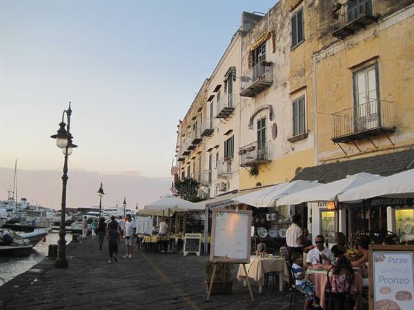 Tourists stroll along the quay past café umbrellas and old waterfront buildings