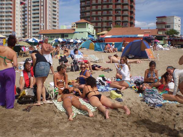 Beachgoers in bikinis and tents on sand, high-rises behind