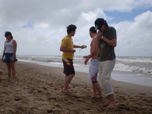 Friends on sandy beach, one taking photos with compact camera, waves behind