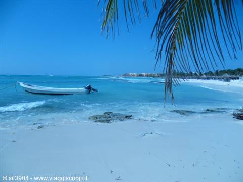 White boat moored on white sand beach, palm frond and turquoise sea