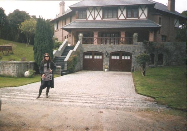 Woman in sunglasses poses in front of a stone and timber villa