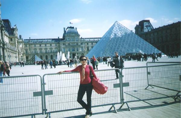 Woman with red bag leaning on a fence in front of the Louvre pyramid