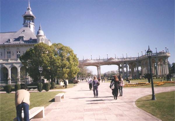 Visitors walk toward a white palace with turret and arcade past gardens