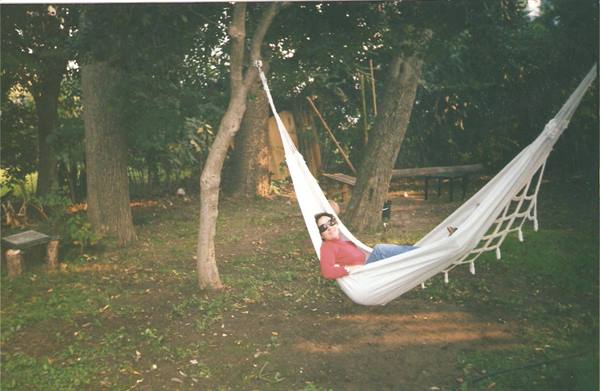 Man in sunglasses relaxing in white hammock strung between garden trees