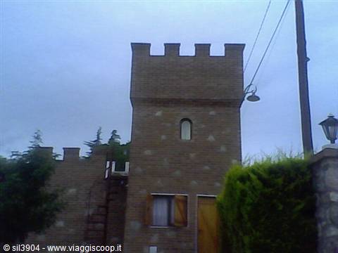 Crenellated brick tower with narrow window, stone walls, overcast sky above