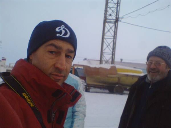 Two smiling men in winter hats near a boat on the snow