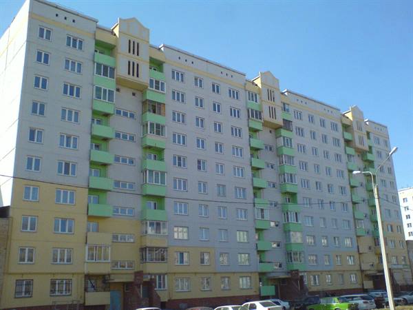 White and green apartment building with balconies, parked cars under blue sky