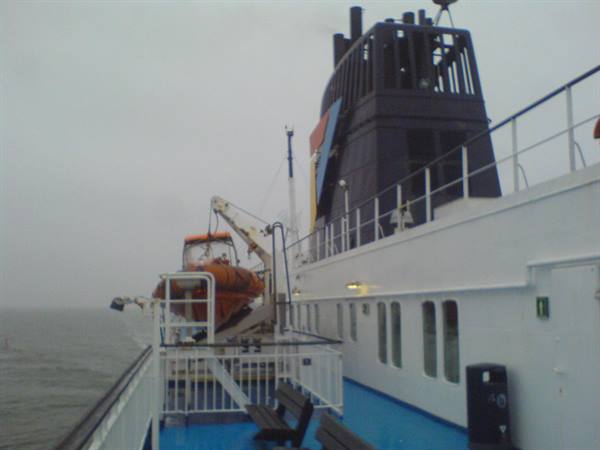 Ferry deck with orange lifeboat and grey sea under overcast sky