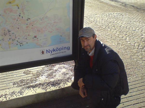 Man crouching beside a Nyköping tourist map on cobblestone pavement