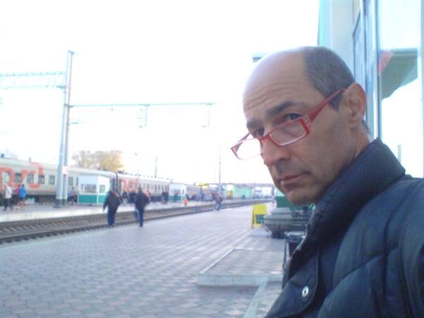 Man with red glasses at station platform, train waiting on tracks
