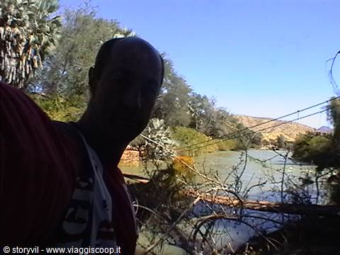 Tourist taking a selfie beside a river with palms and suspension bridge cables
