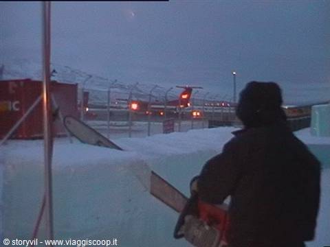 Man with chainsaw cuts snow blocks near fence and lights at dusk