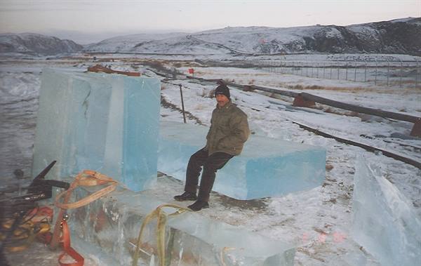 Man sitting on a huge blue ice block in snowy terrain