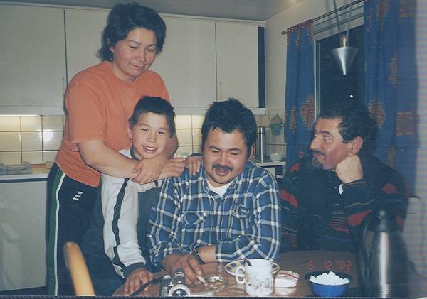 Family gathered around kitchen table, cups and teapot, indoor light