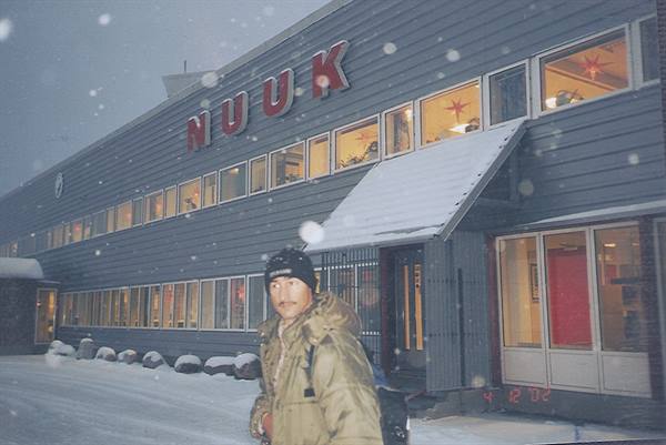 Man in winter coat and hat outside Nuuk shopping center during snowfall