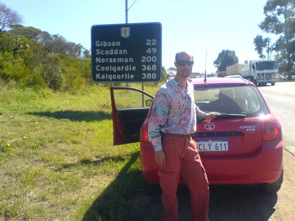 Man beside red Toyota Corolla, road sign showing distances to Norseman and Kalgoorlie