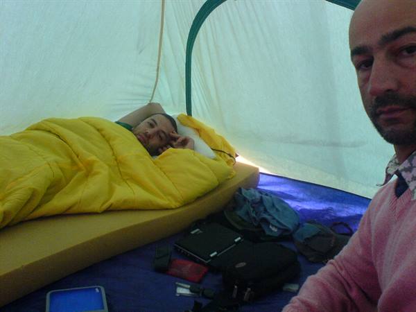 Two men inside a green tent, one sleeping in a yellow sleeping bag