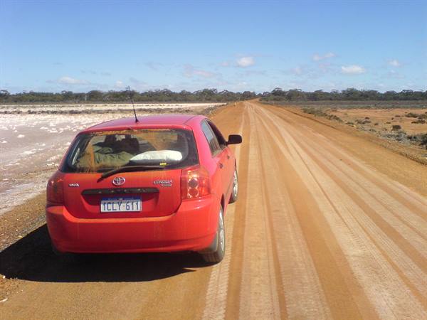 Red Toyota Corolla parked on dirt road beside a salt lake