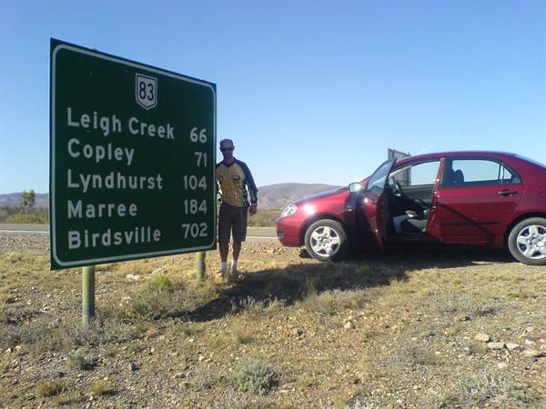 Man beside route 83 road sign to Leigh Creek and Birdsville, red car