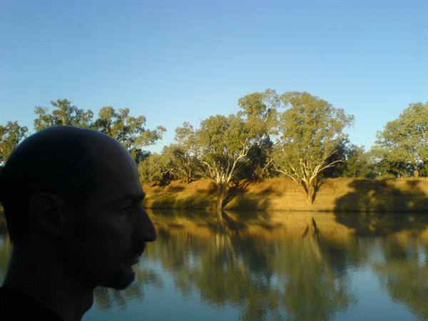 Man's face silhouetted before calm river with eucalyptus trees reflected in water