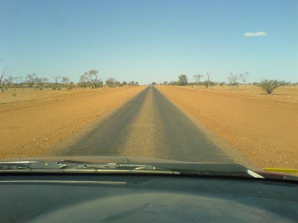 Car on straight outback road, red sand and bushes under blue sky