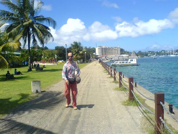 Man walks along pebbled seaside promenade between palms, lawn and ferry pier