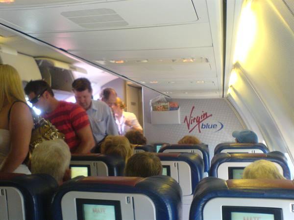 Passengers standing in the aisle of a Virgin Blue airplane cabin