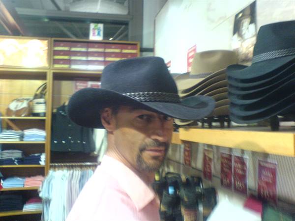 Man wearing black cowboy hat in front of shelves of hats in a store