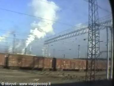 Rusty freight wagons near power pylons and white factory smoke
