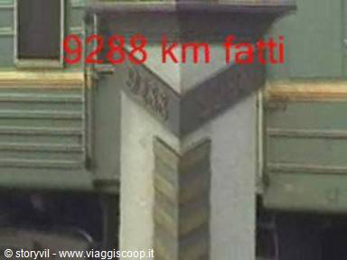 Stone kilometer marker beside a green train wagon, daylight