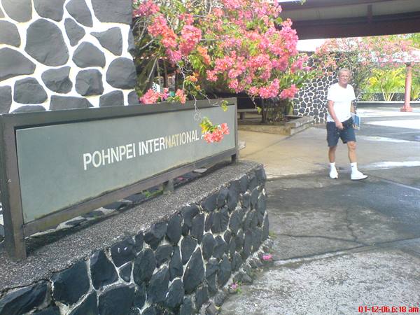 Pohnpei International sign on black stone wall, tourist near pink flowers