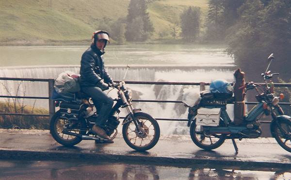 Helmeted rider beside a loaded motorcycle in front of the dam