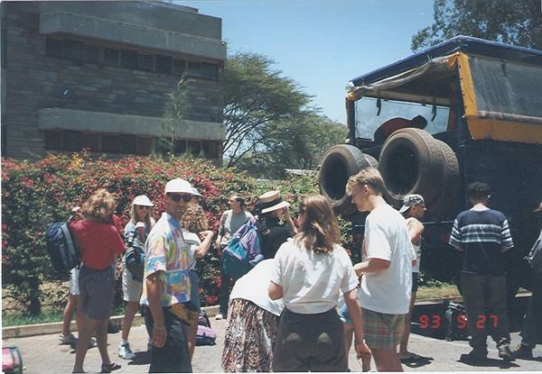 Backpackers load a yellow overland truck with spare tires, red flowers