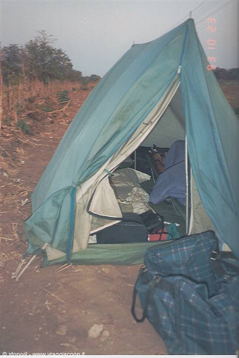 Green tent open on dry ground, backpacks and gear inside, morning light